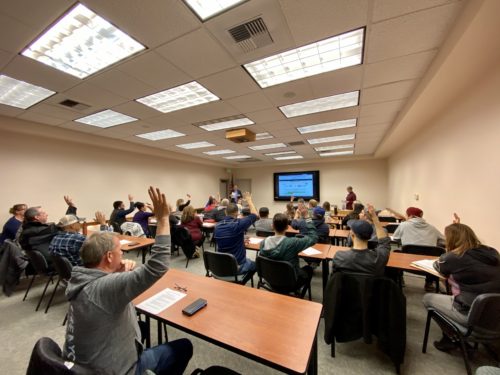 An image of participants in the Enterprise Challenge raising their hands in a classroom-like setting.