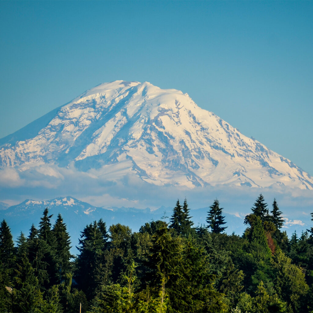 An image of Mount Rainier on a clear day with mist hovering low along the base of the mountain.